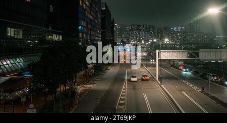 Eine nächtliche urbane Szene mit einer belebten Straße mit mehreren Autos in Hongkong. Stockfoto