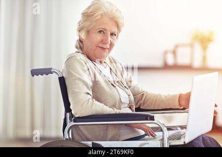 Rollstuhlfahrer, aber sie hat Zugang zum Internet. Eine ältere Frau, die einen Laptop benutzt, während sie im Rollstuhl sitzt. Stockfoto