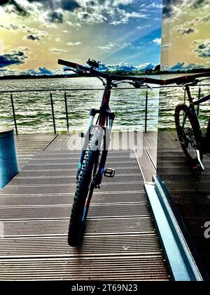 Ein Mountainbike, das auf einem Dock in einen ruhigen See ragt, mit einer friedlichen Landschaft im Hintergrund Stockfoto