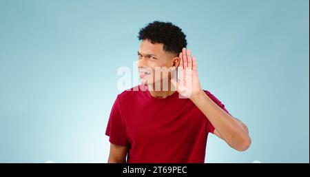 Porträt, Zuhören und Handgeste zum Abhören mit einem Mann, der im Studio auf blauem Hintergrund zuhört. Emoji, Kommunikation und Geheimnis mit einem Stockfoto