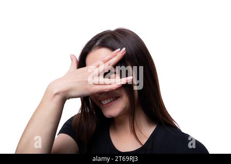 Weiße süße junge Frau mit schwarzen Haaren, die ein schwarzes T-Shirt trägt, ist peinlich und bedeckt ihr Gesicht Stockfoto