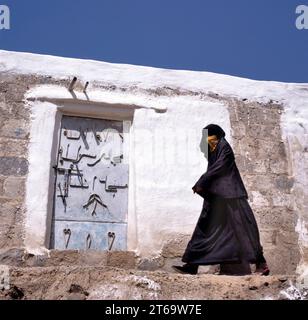 Eine verschleierte muslimische Frau geht auf einer Sanaa Straße im Jemen. Im Hintergrund eine typische Jemen Haustür. Stockfoto