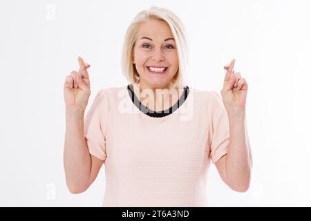 Glückliche Frau mit gekreuzten Fingern isoliert auf weißem Hintergrund, blonde kaukasische Frau mittleren Alters wünscht sich mit gekreuzten Fingern auf weiß Stockfoto