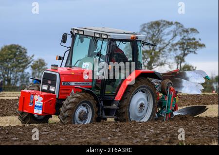 Die Abbildung zeigt einen roten Traktor, der den Boden pflügt, während verschiedene landwirtschaftliche Arbeitsgeräte verwendet werden, um einen Einblick in die Landwirtschaft zu erhalten Stockfoto