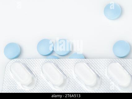 Blisterpackung mit weißen Tabletten über verstreuten blauen Tabletten. Blick von oben. Stockfoto