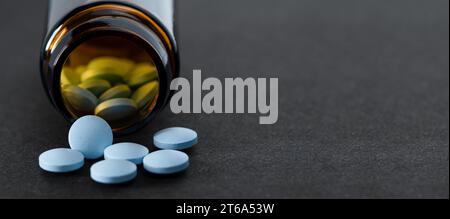 Blaue Pillen, die aus der Pillenflasche auslaufen, auf schwarzem Hintergrund. Stockfoto