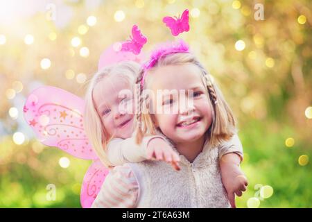 Diese kleine Fee braucht nur Hilfe beim Üben des Fliegens. Porträt von zwei kleinen Schwestern, die als Feen verkleidet sind und draußen Spaß haben. Stockfoto