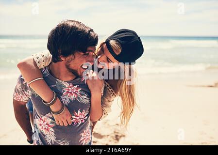 Binding am Strand. Eine attraktive junge Frau, die einen Huckepack von ihrem Freund am Strand bekommt. Stockfoto