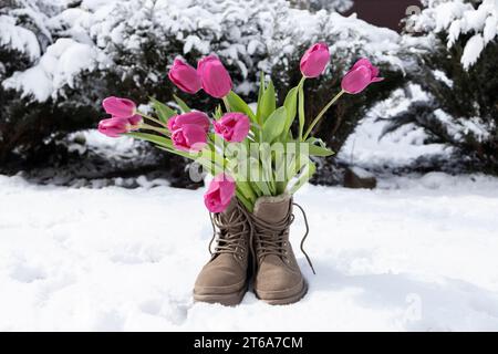 Strauß frischer rosafarbener Tulpen in Stiefeln, stehend auf weißem, frisch gefallenem Schnee. Hi Spring. Zwischen Winter und Frühling. Eine Überraschung für dein geliebtes Mädchen. Stockfoto