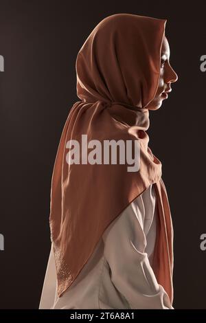 Muslimische Frau, Profil und Hidschab für Religion, islam oder Lob im Glauben vor dunklem Atelierhintergrund. Seitenansicht einer islamischen Frau oder eines islamischen Modells Stockfoto
