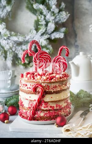 Mehrschichtiger Lebkuchenkuchen mit roten Lolli-Pops, farbigem Konfetti auf weißem Kuchenständer, Weihnachtskugeln, Tannenzweigen auf weißem Beton Stockfoto