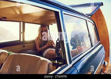 Es ist gemütlich auf dem Rücksitz. Porträt einer glücklichen jungen Frau, die während eines Roadtrips in einem Auto sitzt. Stockfoto