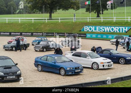 Chester, Cheshire, England, 1. Oktober 2023. Menschen mit Regenschirmen, die auf einer Oldtimer-Auktion einen blauen BMW M3 und einen weißen Mitsubishi EVO V anschauen. Stockfoto