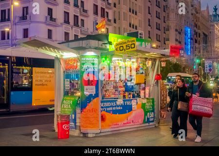 Ein Paar, das in der Nähe eines Kiosks für alkoholfreie Getränke und Süßigkeiten in Callao bei Nacht in Madrid, Spanien, vorbeikam Stockfoto