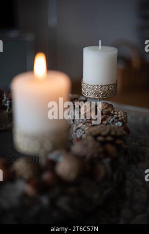 Nahaufnahme von zwei Kerzen in einem Kerzenhalter mit Ornamenten auf einem Adventskranz mit Kegeln und Nüssen Stockfoto