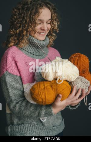 Frau, die in den Händen Plüschstrickgarn auf schwarzem Hintergrund hält. Garn zum Stricken von Spielzeug, Kinder- und Erwachsenenbekleidung, Innenausstattung. Handgefertigt Stockfoto