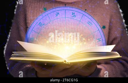 Frau liest Astrologie-Buch auf dunklem Hintergrund, Nahaufnahme Stockfoto