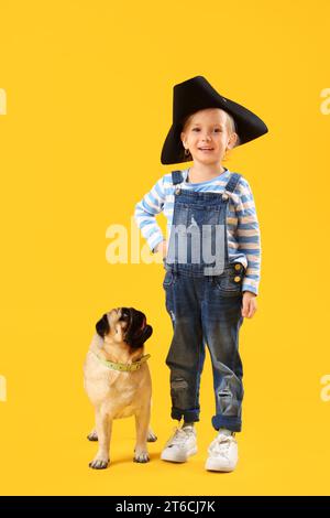 Kleines Mädchen im Piratenhut mit süßem Mops Hund auf gelbem Hintergrund Stockfoto