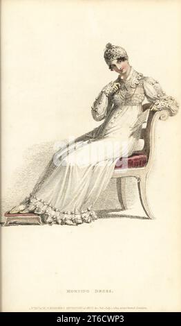 Regency-Frau im Morgenkleid, die einen Brief mit einer Lorgnette liest, auf einem Stuhl mit Fußstütze sitzend, 1814. In rundem Gewand aus feinem Kambric, vorne geknöpft, mit Vandyke-Spitzenbesatz, Baumwoll-Ballfransen, Spitzenkragen, langen Ärmeln mit Ballfransen, orangefarbener Netzkappe, Kinderschuhen mit Primrose. Vol. 12, Platte 3, 1. Juli 1814. Handkolorierter Kupferstich von Thomas Uwins aus Rudolph Ackermanns Repository of Arts, Strand, London. Stockfoto