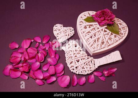 Weidenvogel, zwei Herzen, blühende rote Rose und verstreute Rosenblätter. Stockfoto