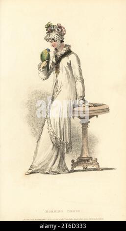 Regency Frau im Morgenkleid spielt mit einem Papagei. In lockerer Robe aus feinem Kambrik über einem Petticoat derselben, mit französischen Besatz geschmeichelte, in einer Vandyke-Ruff geraffte, in Seide eingefasste Taschentücher am Kragen, Mob-Mütze aus Brüsseler Spitze. Vol. 13, Plate 19, 1. April 1815. Handkolorierter Kupferstich von Thomas Uwins aus Rudolph Ackermanns Repository of Arts, Strand, London. Stockfoto