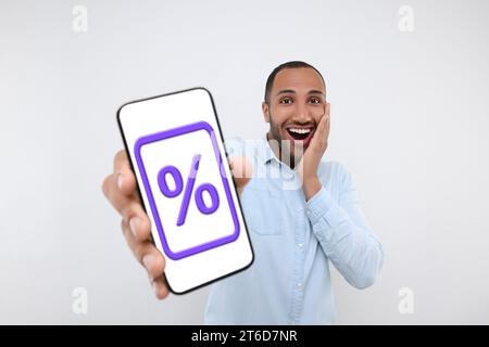 Rabatt, Angebot, Verkauf. Emotionaler Mann zeigt Handy mit Prozentzeichen auf dem Bildschirm, weißer Hintergrund Stockfoto