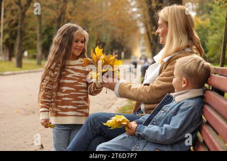 Glückliche Mutter und ihre Kinder verbringen Zeit zusammen mit trockenen Blättern im Herbstpark Stockfoto