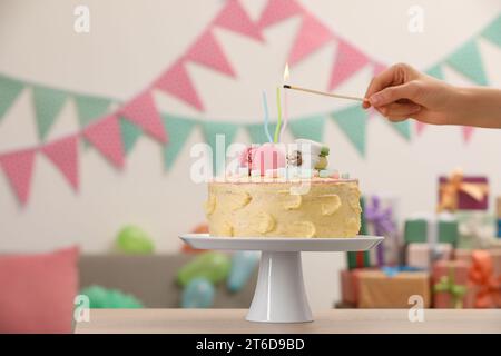 Frau zündet Kerze auf köstlichem Kuchen, dekoriert mit Makronen und Marshmallows im festlichen Raum, Nahaufnahme. Leerzeichen für Text Stockfoto