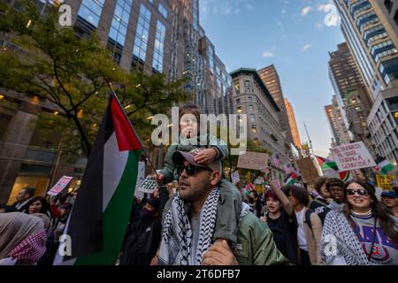 NEW YORK, NEW YORK - 9. NOVEMBER: Ein junger pro-palästinensischer Demonstrant sitzt auf den Schultern eines Mannes, während er während eines Studentenrundgangs durch Midtown Manhattan marschiert, der am 9. November 2023 in New York City zu einem Waffenstillstand zwischen Israel und der Hamas aufruft. Seit dem 7. Oktober hat die israelische Armee die palästinensische Enklave als Vergeltungsmaßnahme für den Angriff der Hamas auf Israel, bei dem über 1.400 Menschen ums Leben kamen, bombardiert, tausende von Gebäuden zerstört, mehr als 10.000 Menschen getötet und 1,4 Millionen vertrieben, während Gaza belagert bleibt. (Foto: Michael Nigro/SIPA USA) Stockfoto