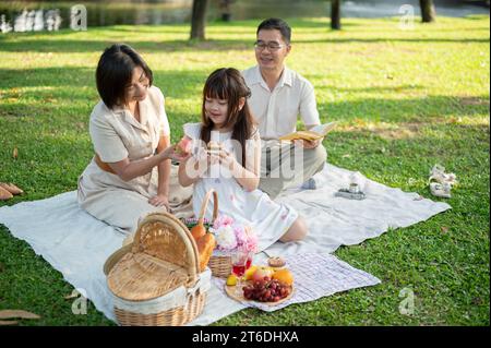 Nette und liebenswerte asiatische Großeltern genießen ein Picknick im Garten mit ihrer entzückenden kleinen Enkelin. Schönes Familienkonzept Stockfoto