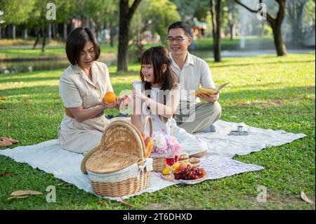 Ein hübsches junges asiatisches Mädchen genießt ein Picknick im grünen Gartenpark mit ihren netten Großeltern und verbringt das Wochenende zusammen. Familienbindung, hap Stockfoto