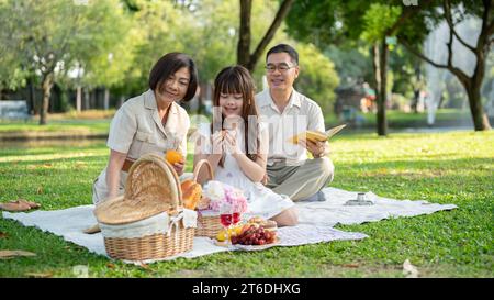 Ein hübsches junges asiatisches Mädchen genießt ein Picknick im grünen Gartenpark mit ihren netten Großeltern und verbringt das Wochenende zusammen. Familienbindung, hap Stockfoto