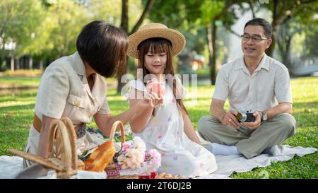 Ein entzückendes junges asiatisches Mädchen redet gerne mit ihrer Großmutter und ihrem Opa, während sie gemeinsam in einem grünen Park picknickt. Familienverbund-Konzept, großartig Stockfoto