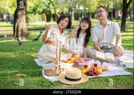 Glückliche asiatische Großeltern und Enkelin haben gemeinsam Spaß im grünen öffentlichen Park und picknicken am Wochenende. Familienurlaub, Familienverbindung Stockfoto