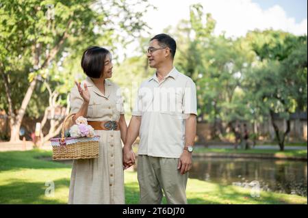 Glückliche asiatische Seniorenpaare unterhalten sich gerne, während sie an einem Sommertag durch den grünen Park schlendern und Zeit miteinander verbringen. Glückliches Heiratsleben, Stockfoto