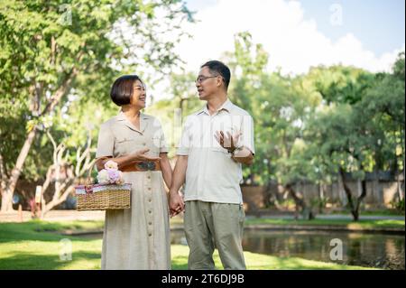 Glückliche asiatische Seniorenpaare unterhalten sich gerne, während sie an einem Sommertag durch den grünen Park schlendern und Zeit miteinander verbringen. Glückliches Heiratsleben, Stockfoto