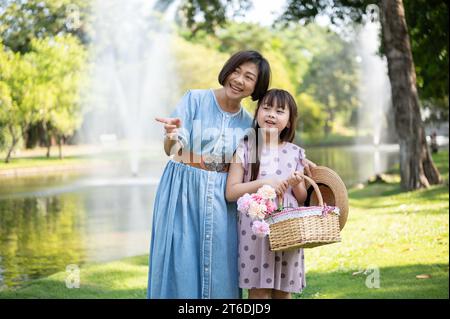 Eine glückliche und freundliche asiatische Großmutter spaziert und hat am Wochenende Spaß im grünen Park mit ihrer reizenden Enkelin. Freizeit und Familienbindung Stockfoto