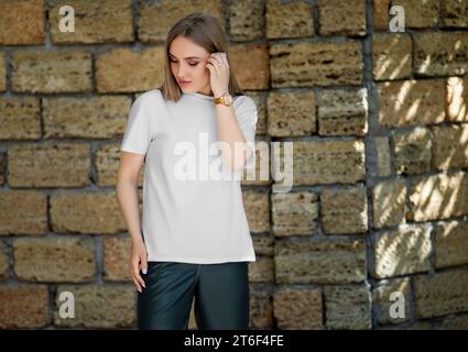 Vorlage eines weißen T-Shirts auf einem posierenden Mädchen, auf dem Hintergrund einer Backsteinmauer mit Schatten, für Branding, Design. Produktfotografie. Modell eines s Stockfoto