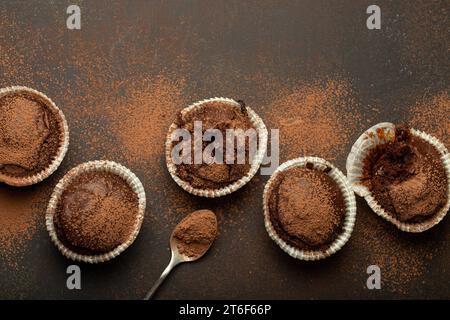 Schokoladen-braune Muffins und Kakao in Teelöffel von oben auf braunem rustikalem Steinhintergrund, süße hausgemachte dunkle Schokolade Cupcakes Stockfoto