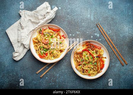 Zwei Schüsseln mit Chow mein oder Lo mein, traditionellen chinesischen Pfannennudeln mit Fleisch und Gemüse, serviert mit Essstäbchen von oben auf rustikalem Blau Stockfoto