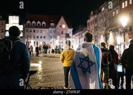 Klang der Stolpersteine Jena eine politisch-künstlerische Aktion Jenaer Bürger, zwar initiiert und koordiniert von Klaus Wegener, Prof. Gerhard Paulus und Till Noack, aber getragen von über 400 Künstlerinnen und Künstlern aus Jena und Umgebung und fast 100 weitere HelferInnen. 9. November, dem Tag der Reichspogromnacht 1938, findet diese in Jena an den Stolpersteinen statt. Eine Person hat sich auf dem Marktplatz in Jena eine große Israel Flagge umgehängt Innenstadt *** Klang der Stolpersteine Jena Eine politisch künstlerische Aktion Jenaer Bürger, initiiert und koordiniert von Klaus Wegener Stockfoto