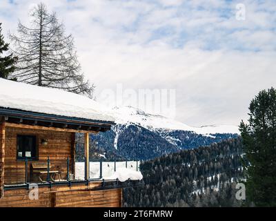 Blick von außen auf den Balkon eines Hotel-Apartment-Chalets in einem Skigebiet im Winter, mit Kiefernwald und Berggipfel im Hintergrund, Kärnten, Austri Stockfoto