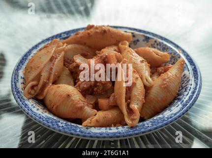 Pasta-Conchiglioni in Form von Muscheln mit gehackter Tomatensauce aus Schweinefleisch auf einer Keramikplatte. Nudelschalen, Platz für Text, selektiver Fokus. Stockfoto