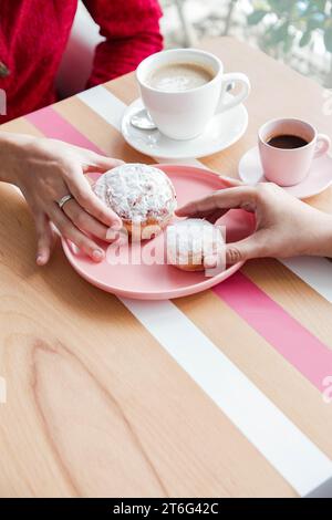 Zwei Frauen halten rosa Jelly Donuts drinnen in der Hochwinkelansicht im Café Stockfoto