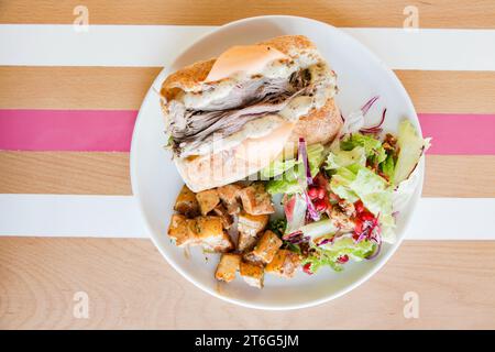 Sandwich mit offenem Roastbeef auf einem Teller serviert mit Gemüse an der Seite auf einem Holztisch mit Streifen. Stockfoto