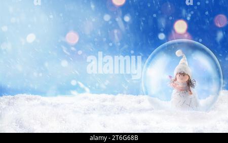 Weihnachtsschneekugel mit einem kleinen süßen Engel auf Schnee draußen Stockfoto