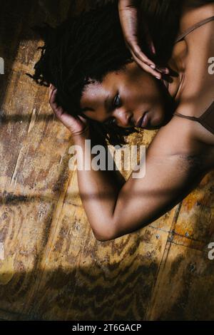 Schwarzes weibliches Gesicht liegt auf Holzboden mit direkter Fensterbeleuchtung Stockfoto