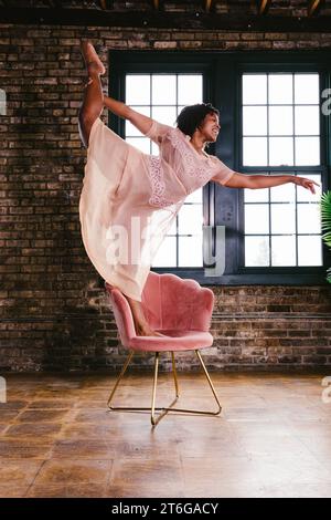 Schwarze Tänzerin in stehender geteilter Pose auf Stuhl im Kleid Stockfoto