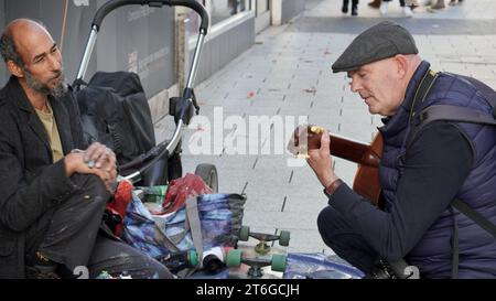 Ein Straßenkünstler, Finger in Sprühfarbe eingeklemmt, plaudert mit einem Straßenfotografen, der die Gitarre spielt, die er für Busking benutzt, und sich gegenseitig Gesellschaft genießt Stockfoto