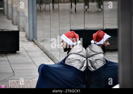 Elend im Stadtzentrum von Cardiff. Ein Obdachloser mit einem Schild und einem weihnachtsmann-Hut sitzt unter einer Decke in der Eingangspassage von John Lewis Betteln Stockfoto